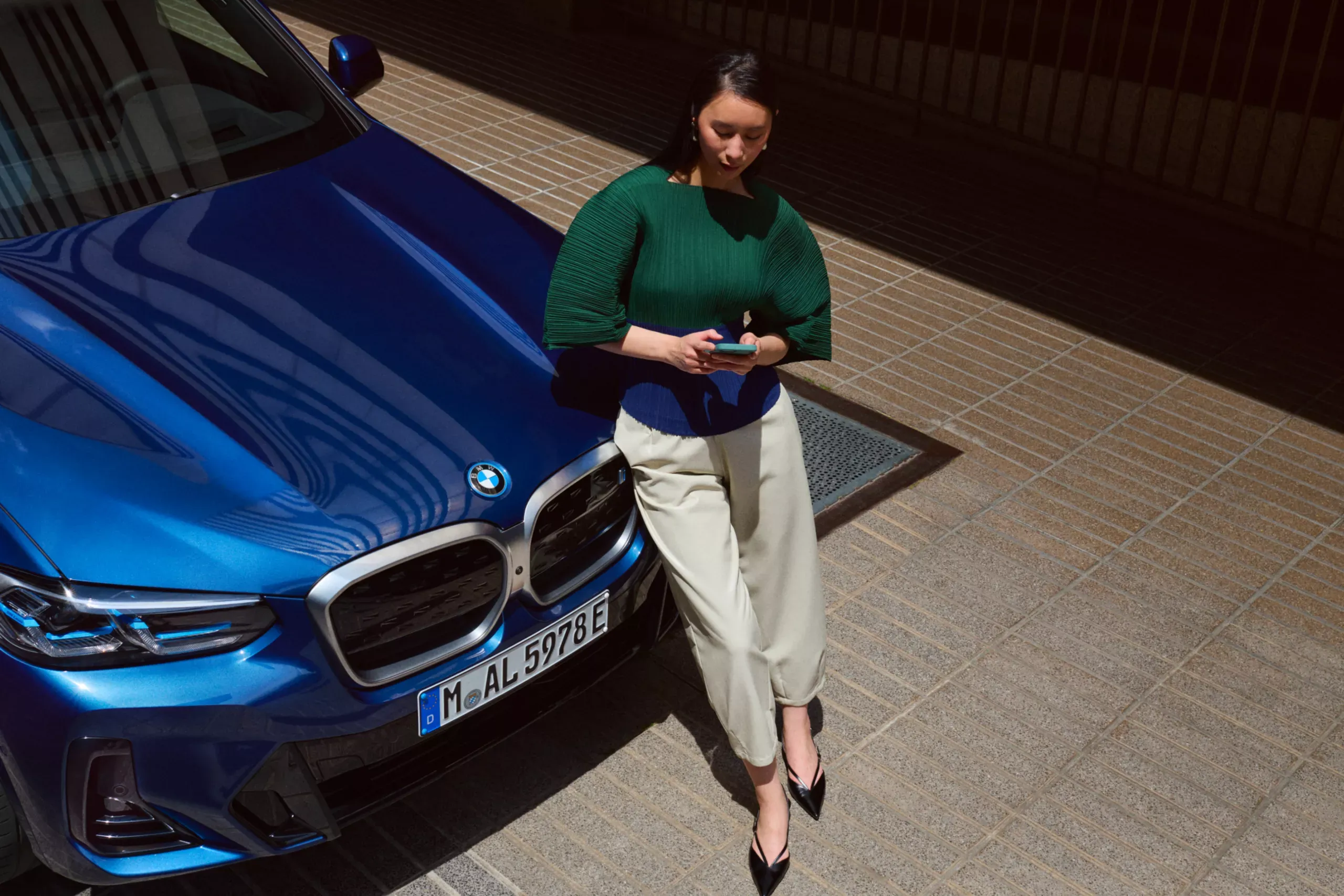 Professionnel consultant son téléphone appuyé sur le capot d'une BMW.
