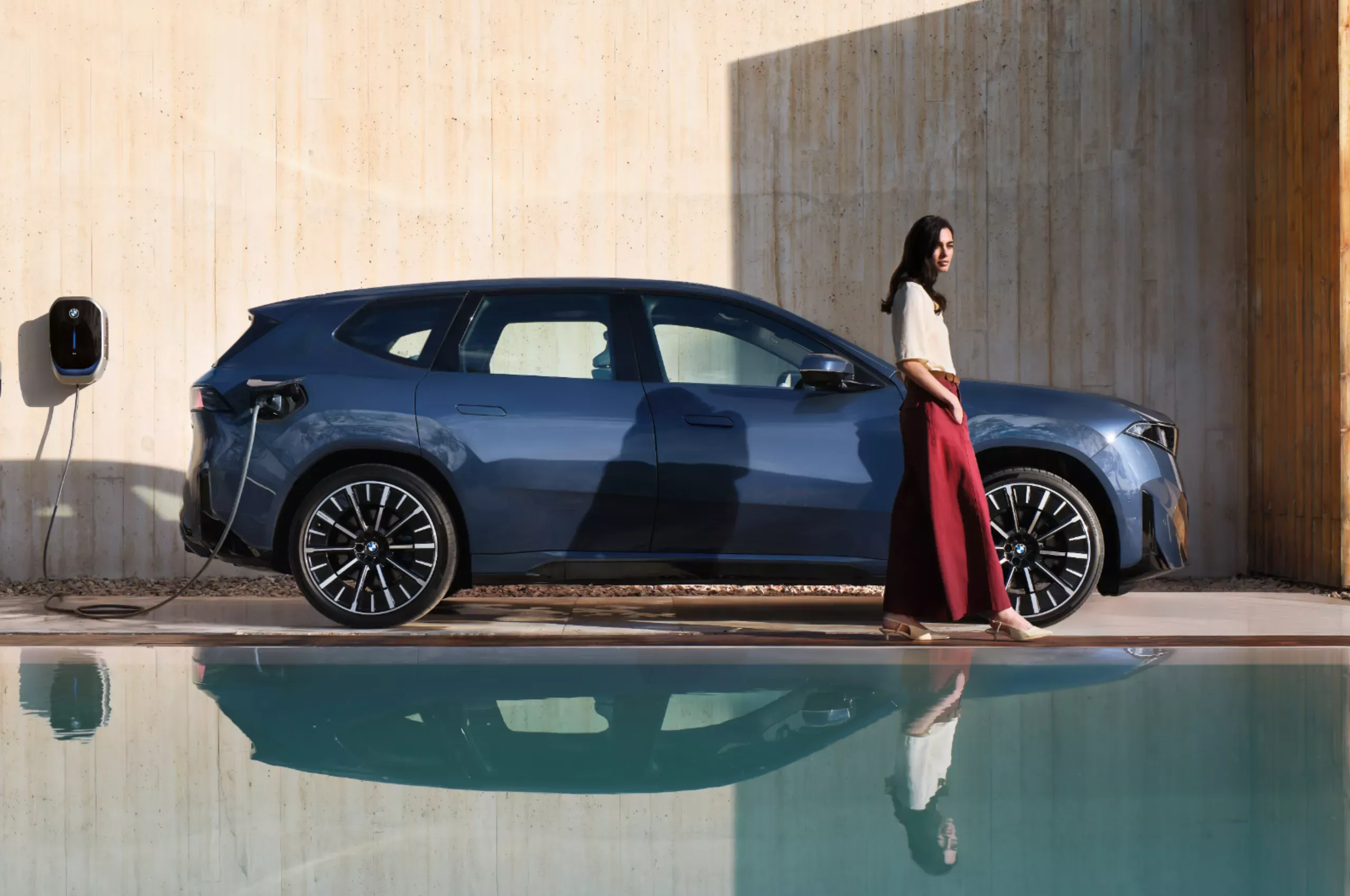 BMW réfléchie dans un étang devant une borne de recharge murale.
