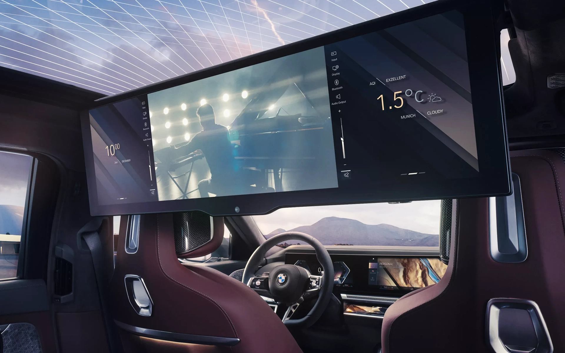 Rear cinema-style display integrated in a BMW, showing multimedia content and weather data, as seen from the passenger seats.