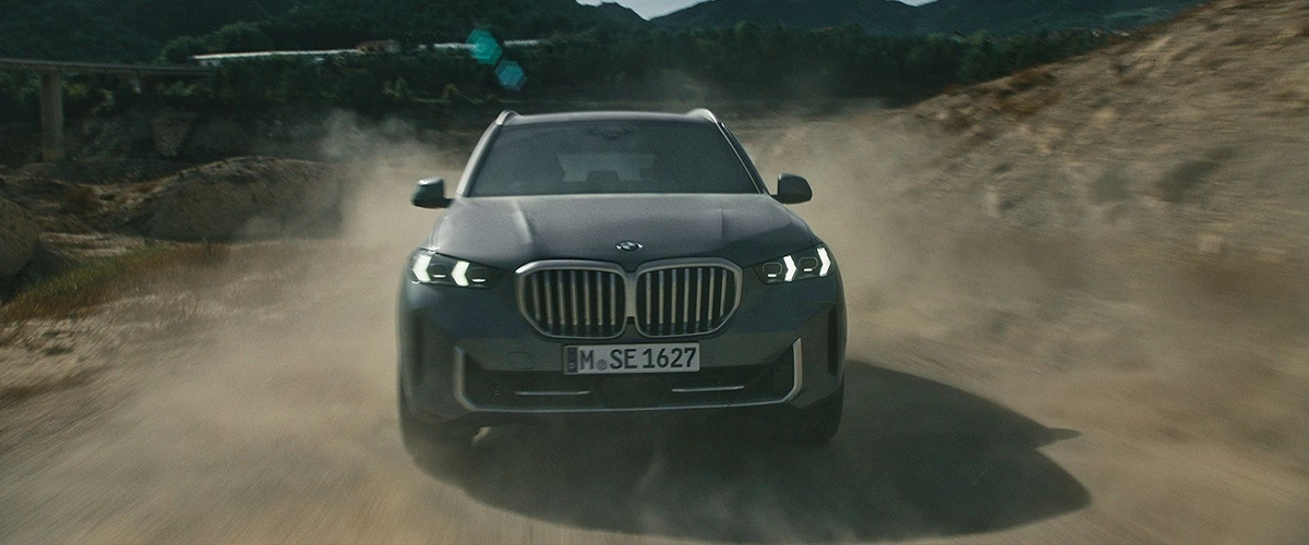 Front view of 2025 BMW X5 driving on a desert road, emphasizing front grille design.
