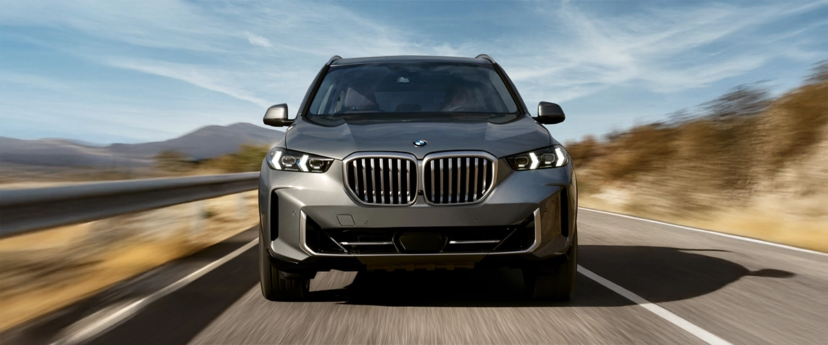 Front view of 2025 BMW X5 driving on a desert road, emphasizing front grille design