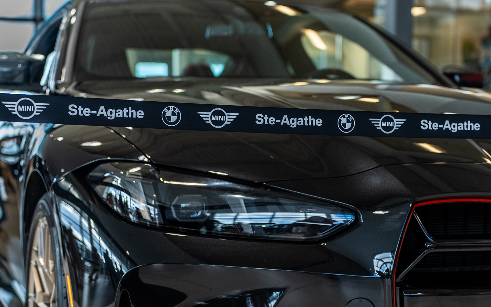 Close-up of a black BMW sports car showcased at an event at BMW | MINI Ste-Agathe, with a branded ribbon featuring BMW and MINI logos.