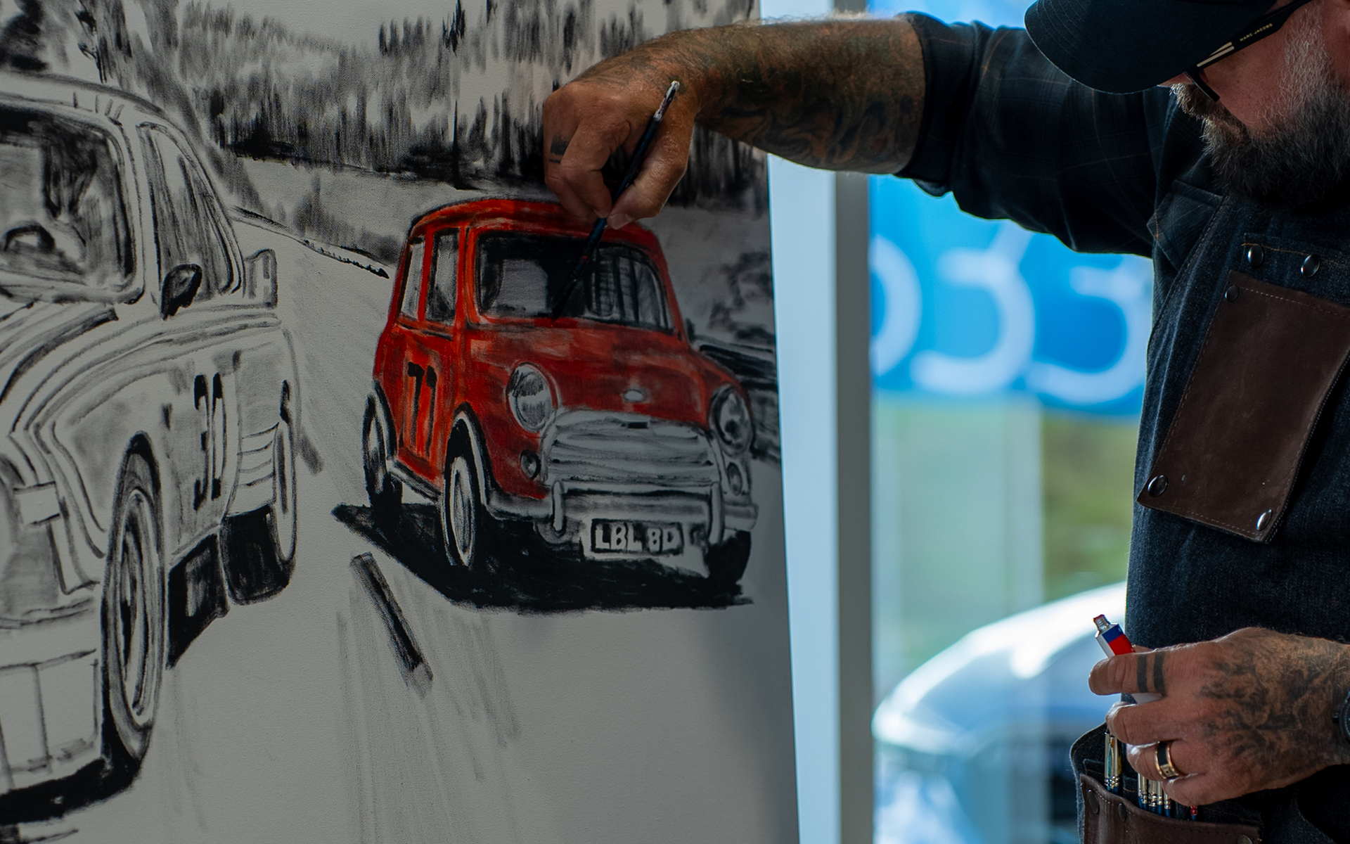 Artist painting a racing scene with a red MINI on a wall.