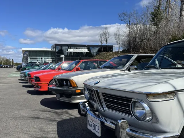 BMW 2002 blanche au premier plan d’une rangée de BMW de collection, devant la concession.